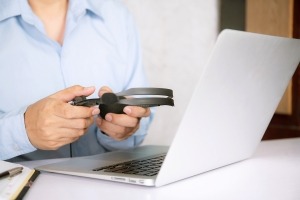 Ein Mann hält einen Kopfhörer in der Hand, während ein Laptop auf dem Schreibtisch neben ihm steht.
