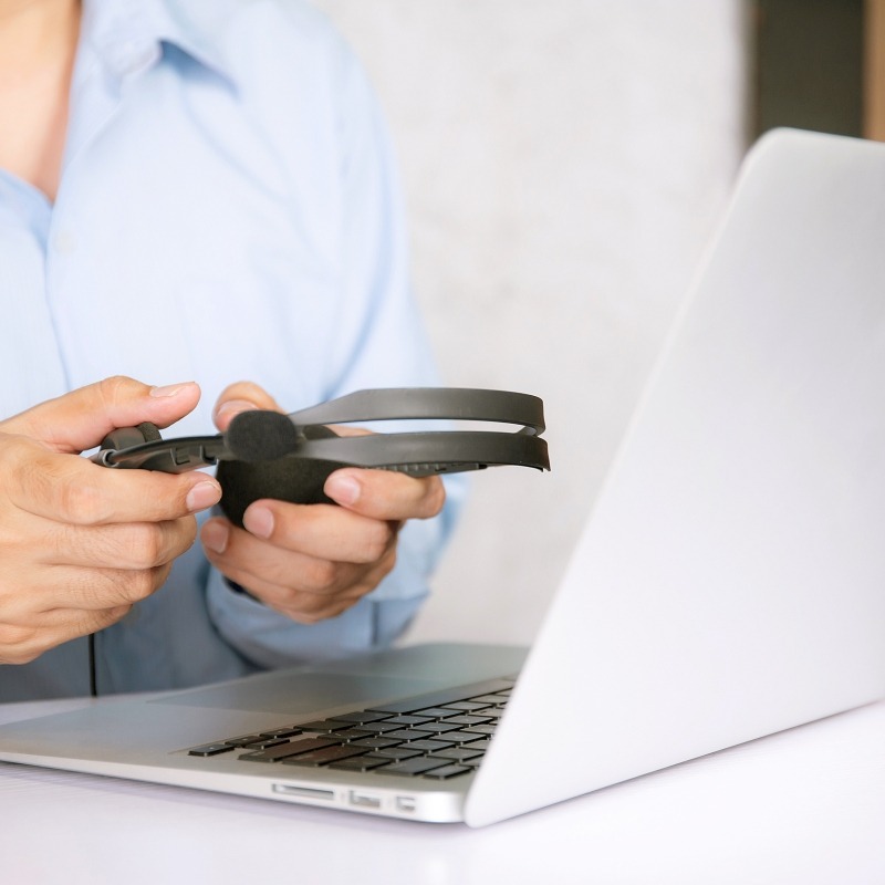 Ein Mann hält einen Kopfhörer in der Hand, während ein Laptop auf dem Schreibtisch neben ihm steht.